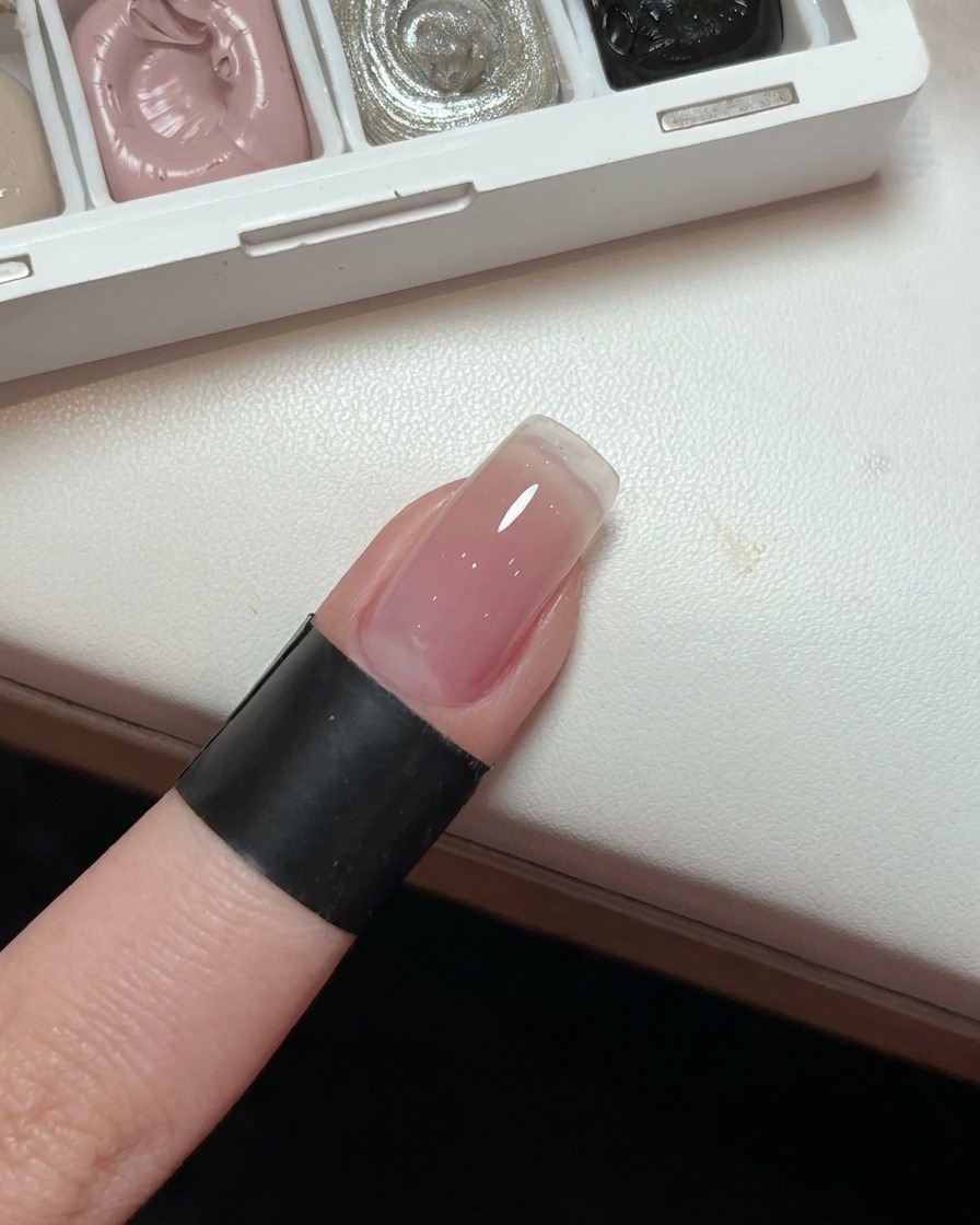 Un primo piano di ununghia che mostra una base in gel sfumata rosa chiaro e uniforme.