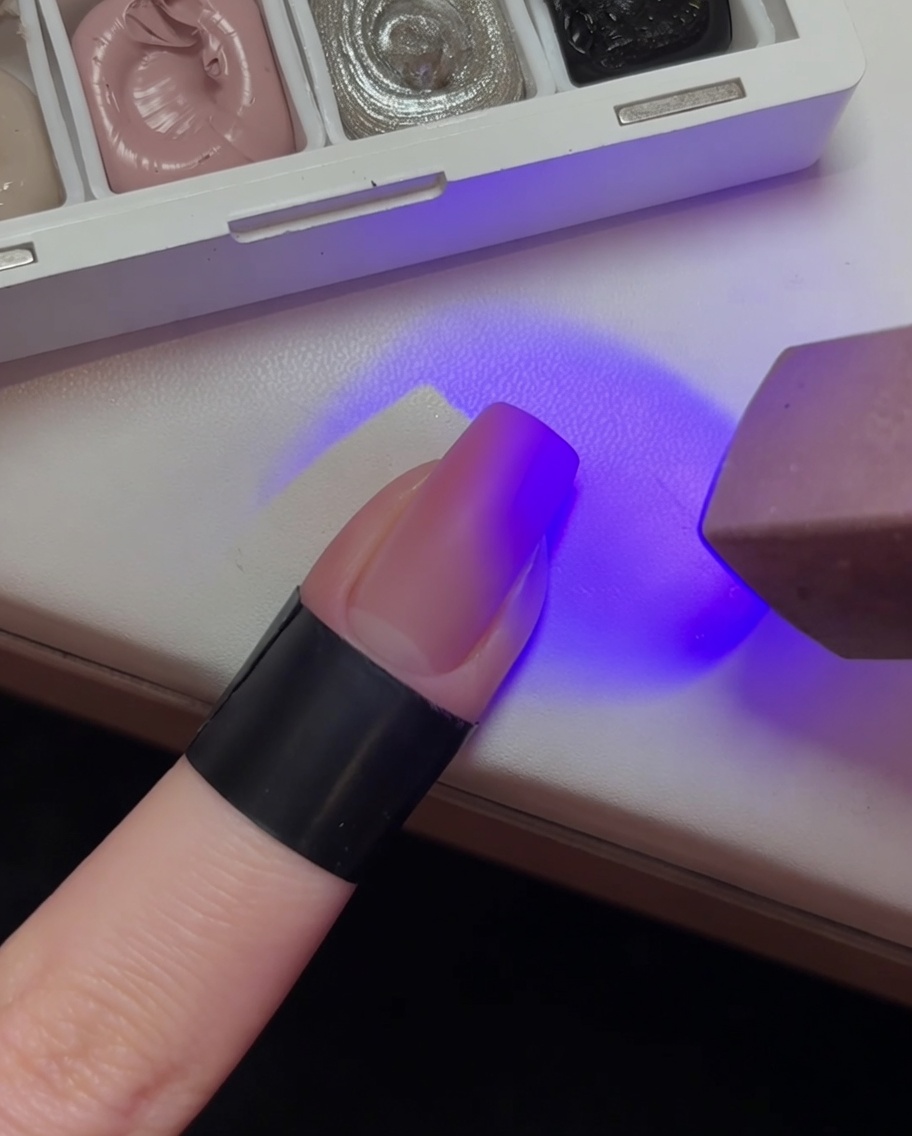 Ununghia con una base sfumata rosa chiaro in fase di polimerizzazione sotto la luce viola di una lampada UV.