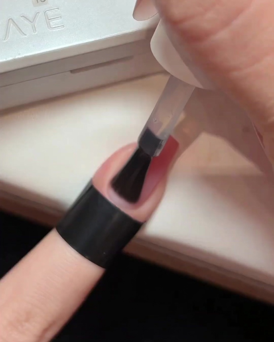 Un pennello che applica uno strato di top coat trasparente e lucido su ununghia sfumata rosa.