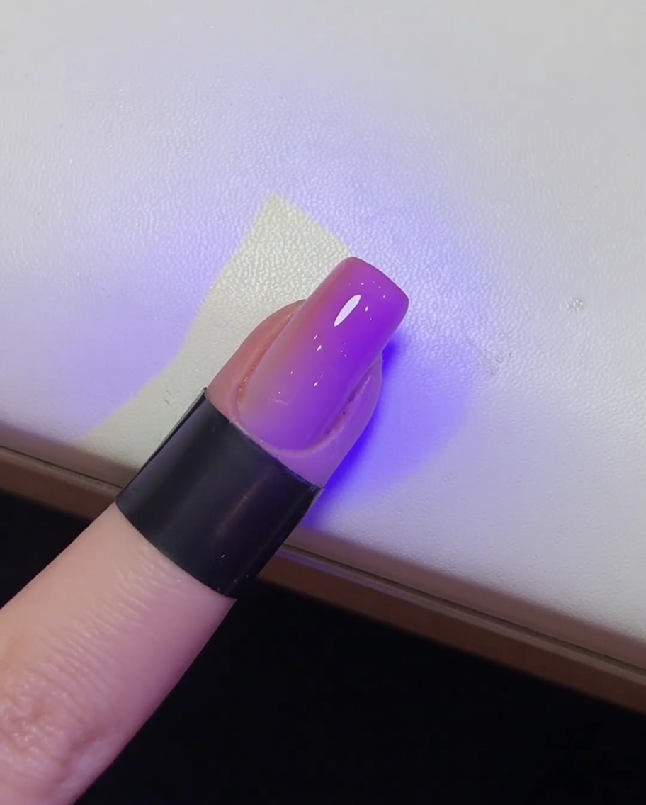 Un primo piano di ununghia lucida finita in fase di polimerizzazione sotto una lampada UV.