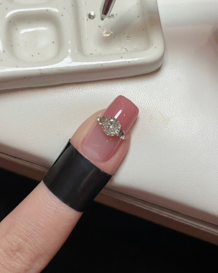 Un primo piano di ununghia con un grande cristallo, che mostra uno strumento di precisione che posiziona minuscole perline dacciaio attorno alla base per creare un effetto a griffe.