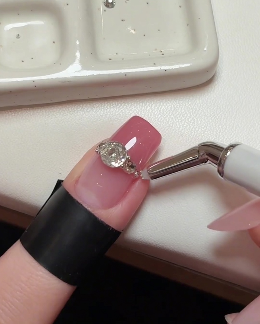 Uno scatto dettagliato della nail art, che mostra uno strumento di precisione che inserisce perline dacciaio microscopiche nei piccoli spazi tra i cristalli più grandi.