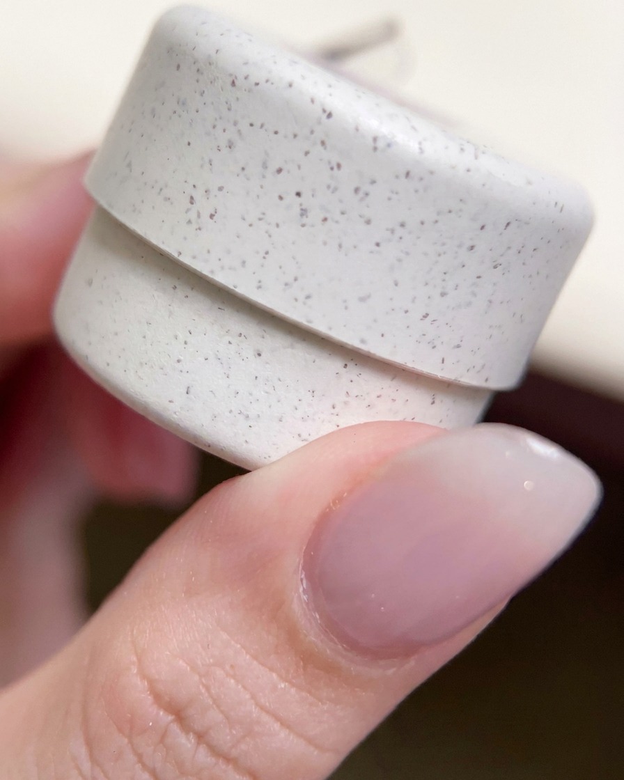 Un primo piano della mano che tiene il vasetto decorato di smalto gel, pieno di particelle glitterate.