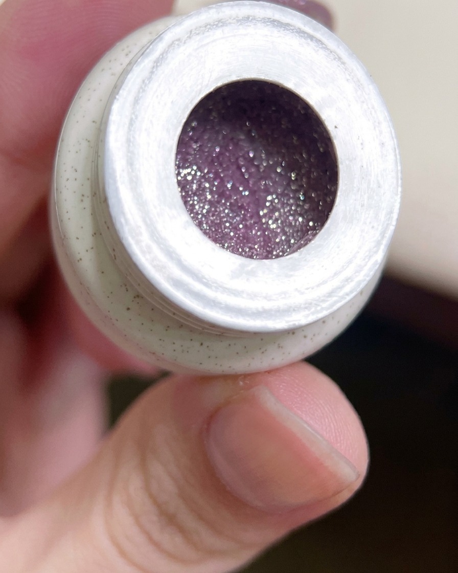 Un pennello piatto da gel che preleva una piccola quantità di smalto gel viola glitterato dal vasetto.
