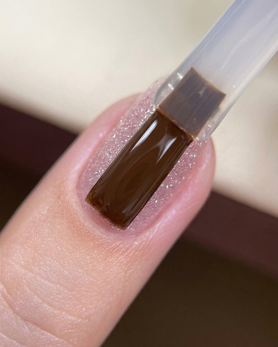 Un pennello da gel che applica un top coat trasparente e lucido sopra ununghia coperta di glitter.