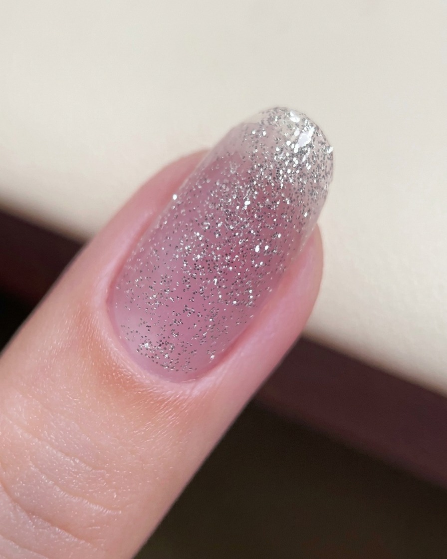 Un primo piano di ununghia con un sottile strato di base di gel glitterato applicato.