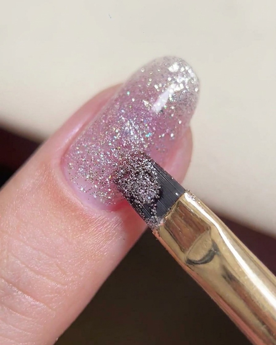 Un pennello da gel che manipola una goccia più grande di gel glitterato al centro dellunghia.