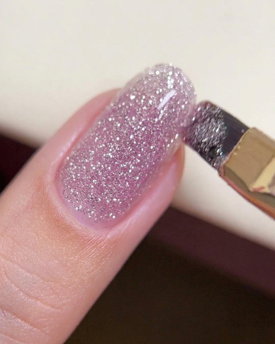 Un pennello che fa scivolare una goccia più spessa di gel crushed diamond attraverso il centro di ununghia per creare uno strato uniforme.