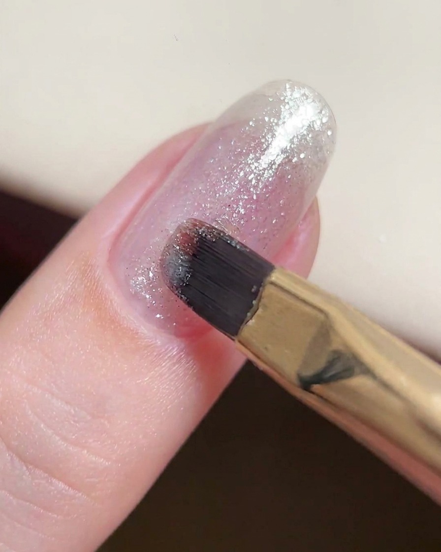 Un pennello da gel che applica uno strato sottile e consistente di gel glitter argento fine su ununghia naturale.