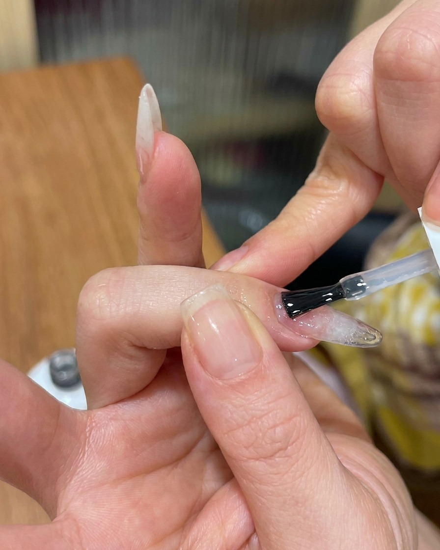 Un pennello applica un top coat trasparente e lucido su ununghia in gel cat-eye strutturata.
