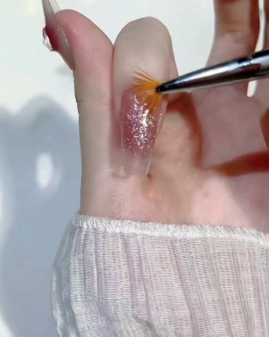 Un piccolo pennello a ventaglio che sfiora leggermente lo strato bagnato di gel glitter su ununghia.