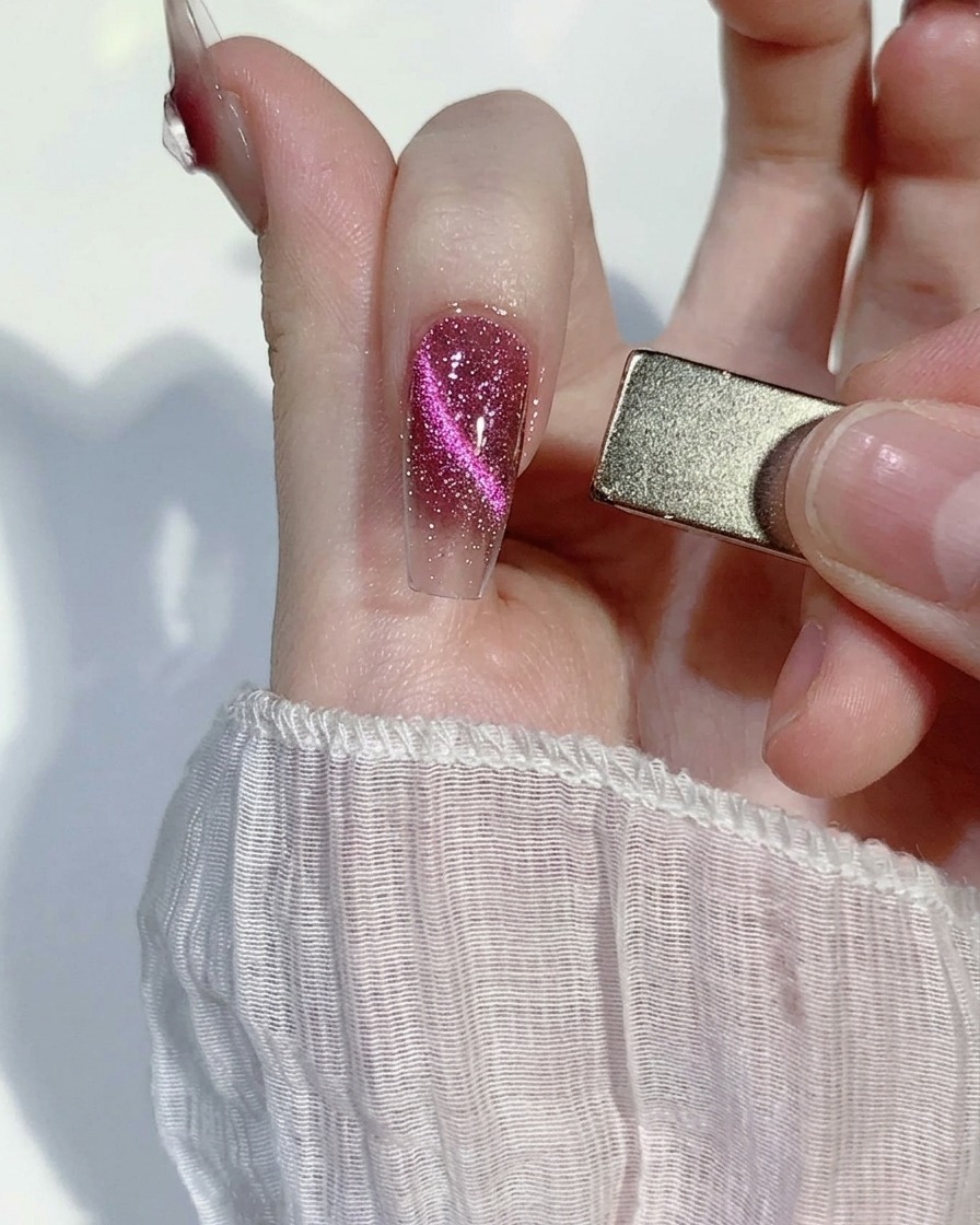 Un magnete rettangolare tenuto di lato vicino a ununghia glitterata rosa, attirando le particelle in una linea definita.