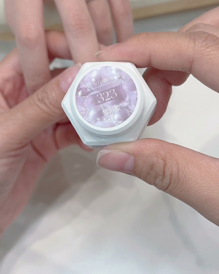 Un pennello applica uno strato di gel cat-eye dai toni chiari su ununghia.