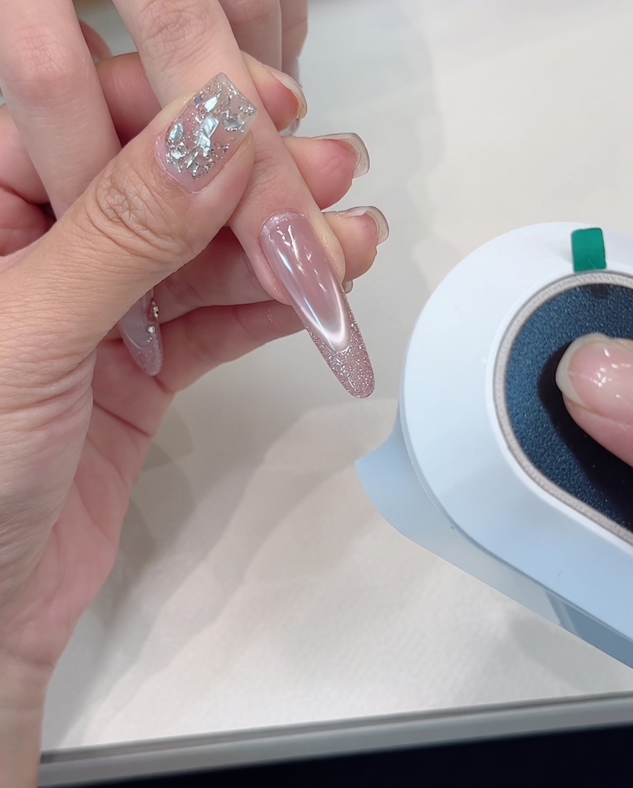 Una mano posizionata sotto una lampada per unghie, con il focus sulle unghie con punta glitterata.