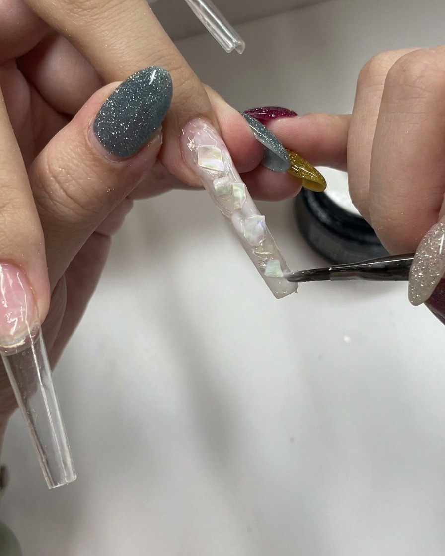 Un pennello applica uno strato di gel bianco latte velato su una superficie ruvida con conchiglie.
