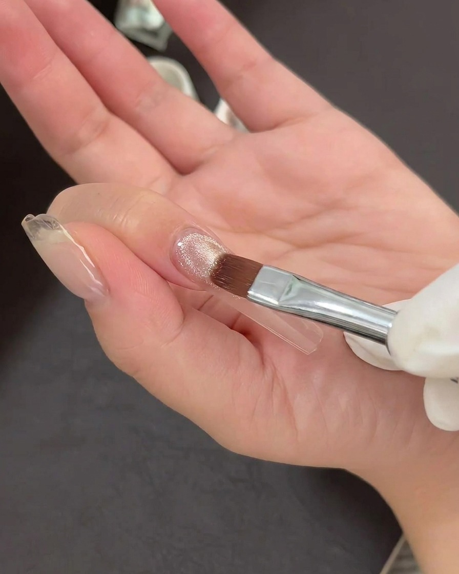 Un pennello da nail art applica uno strato sottile di gel cat-eye brillante su una tip trasparente.