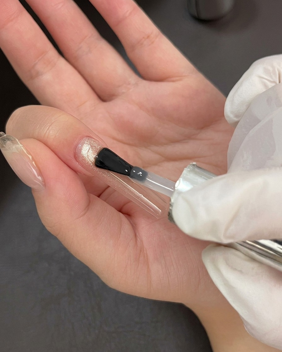 Un pennello da unghie professionale applica un top coat trasparente e lucido sopra la base cat-eye.