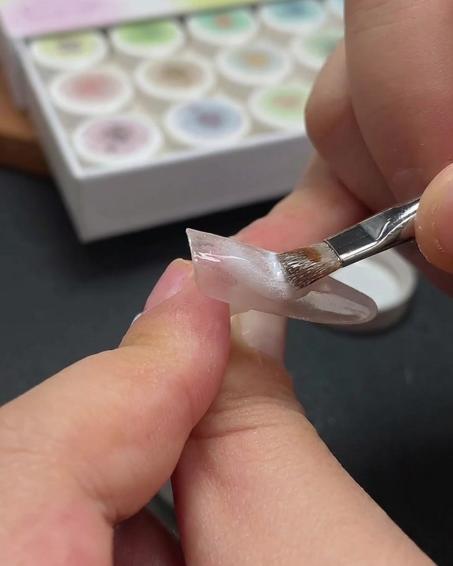 Primo piano che mostra una bacchetta magnetica sospesa sopra ununghia per spostare le particelle metalliche nel gel cat-eye bianco bagnato.
