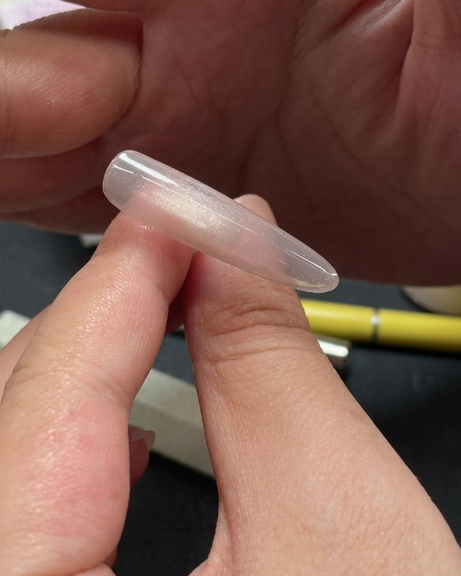 Primo piano di una mano che usa uno strumento per posizionare piccoli pezzi di glitter scintillante sulla parte superiore di ununghia cat-eye.