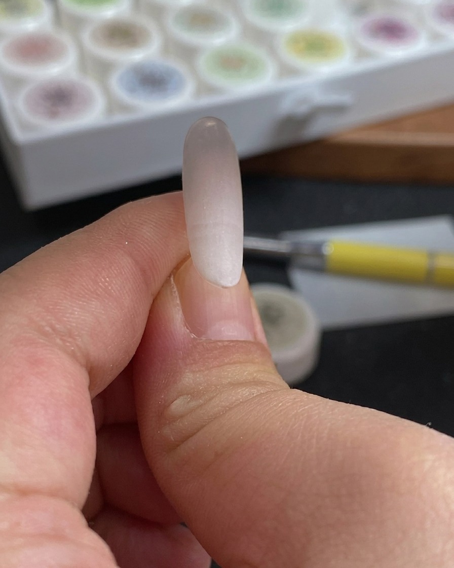 Primo piano di una spugna che viene tamponata sulla punta di ununghia per creare una sfumatura morbida bianco e rosso rosato.