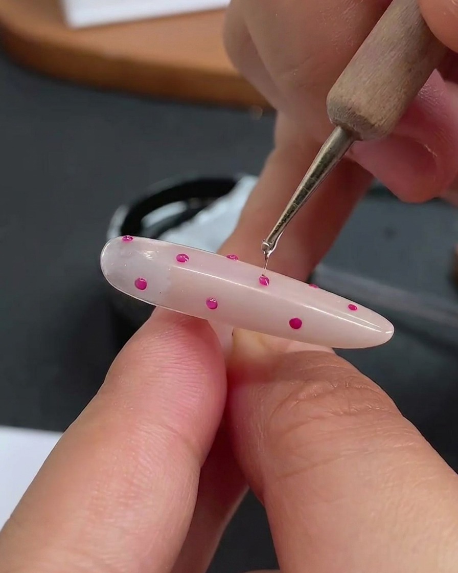 Uno strumento a punta sferica che applica una piccola goccia trasparente di hard gel sopra ogni singolo pois.