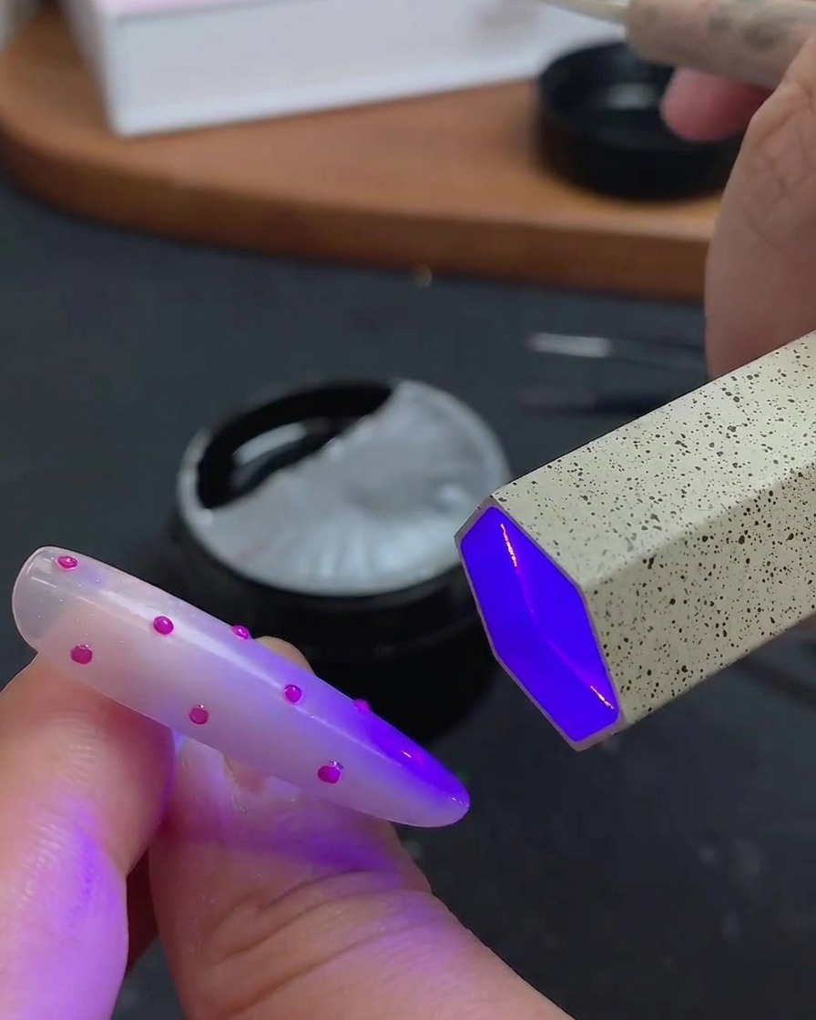 Un pennello che applica un top coat trasparente e lucido sulla nail art 3D a pois.