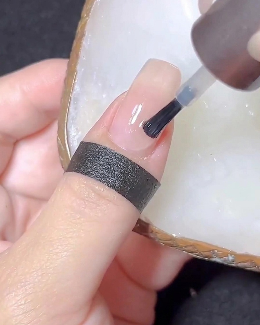 Un pennello per unghie che applica un top coat trasparente su ununghia color nude.