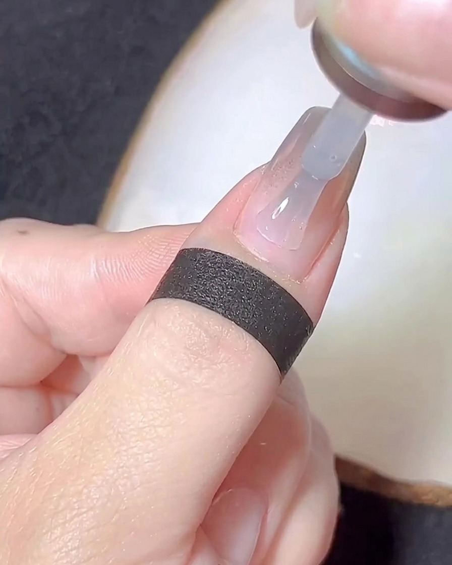 Un pennello che applica un sottile strato di base gel trasparente su ununghia con polvere cromata.