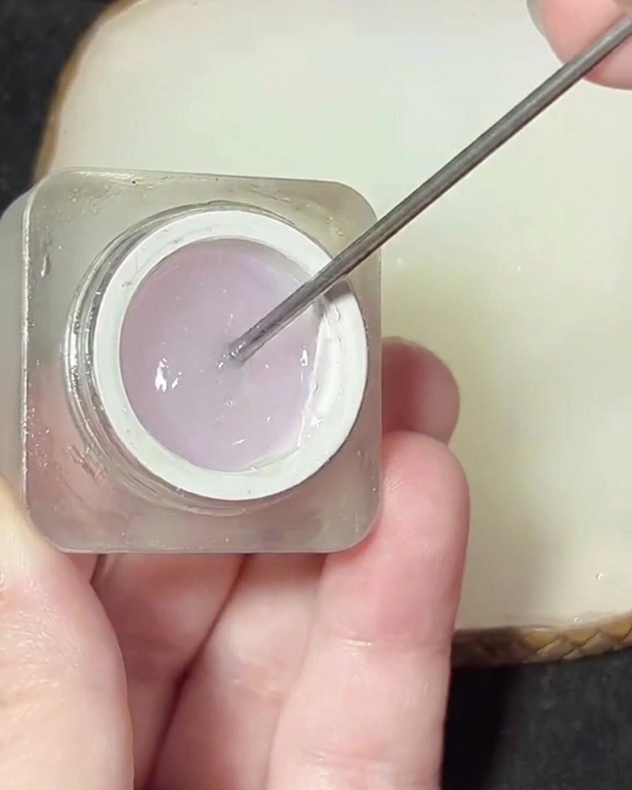 Una spatola in metallo che preleva una piccola quantità di gel denso e trasparente da un vasetto.