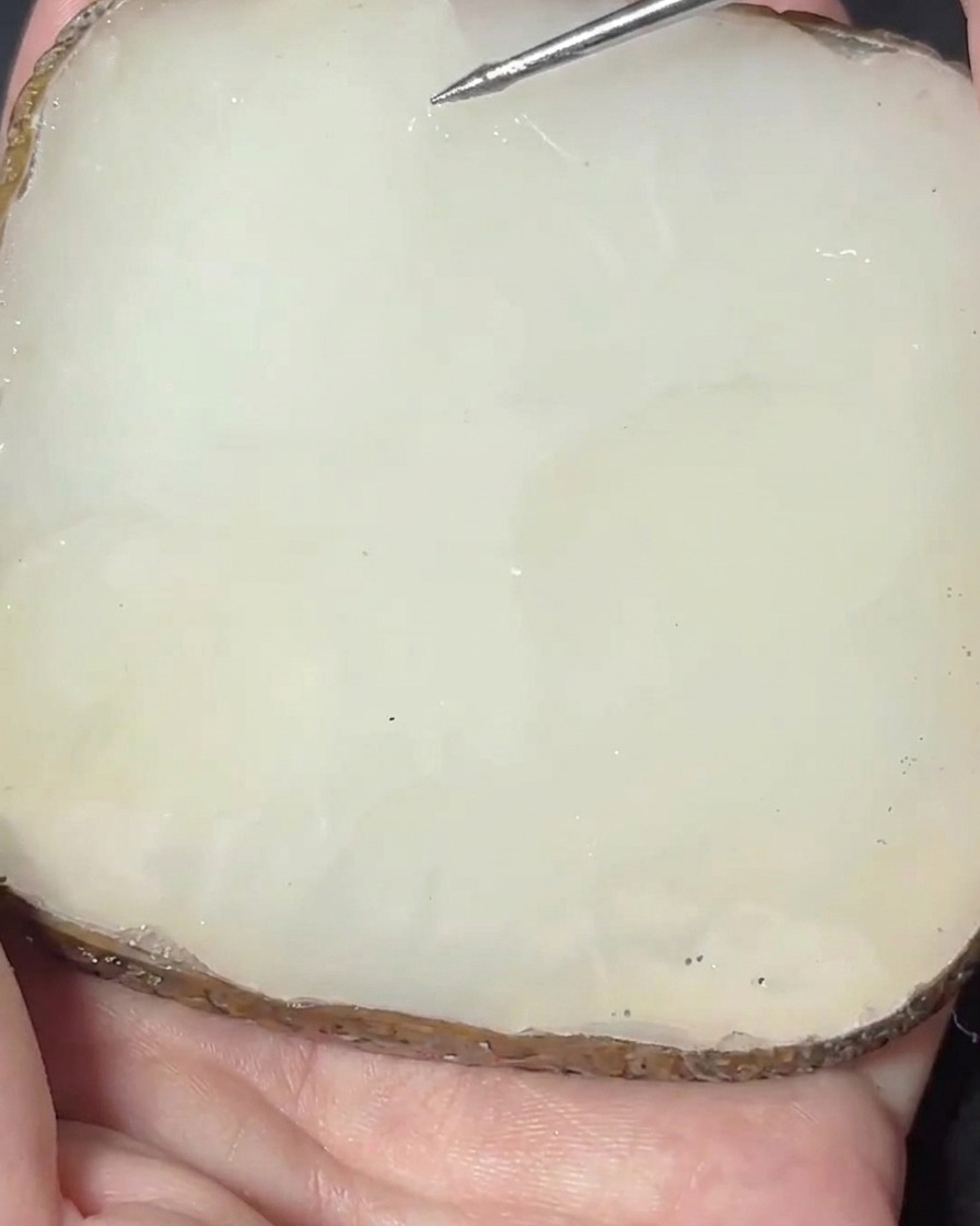 Una spatola in metallo che mescola un pigmento rosa in una base gel trasparente su una tavolozza di pietra.