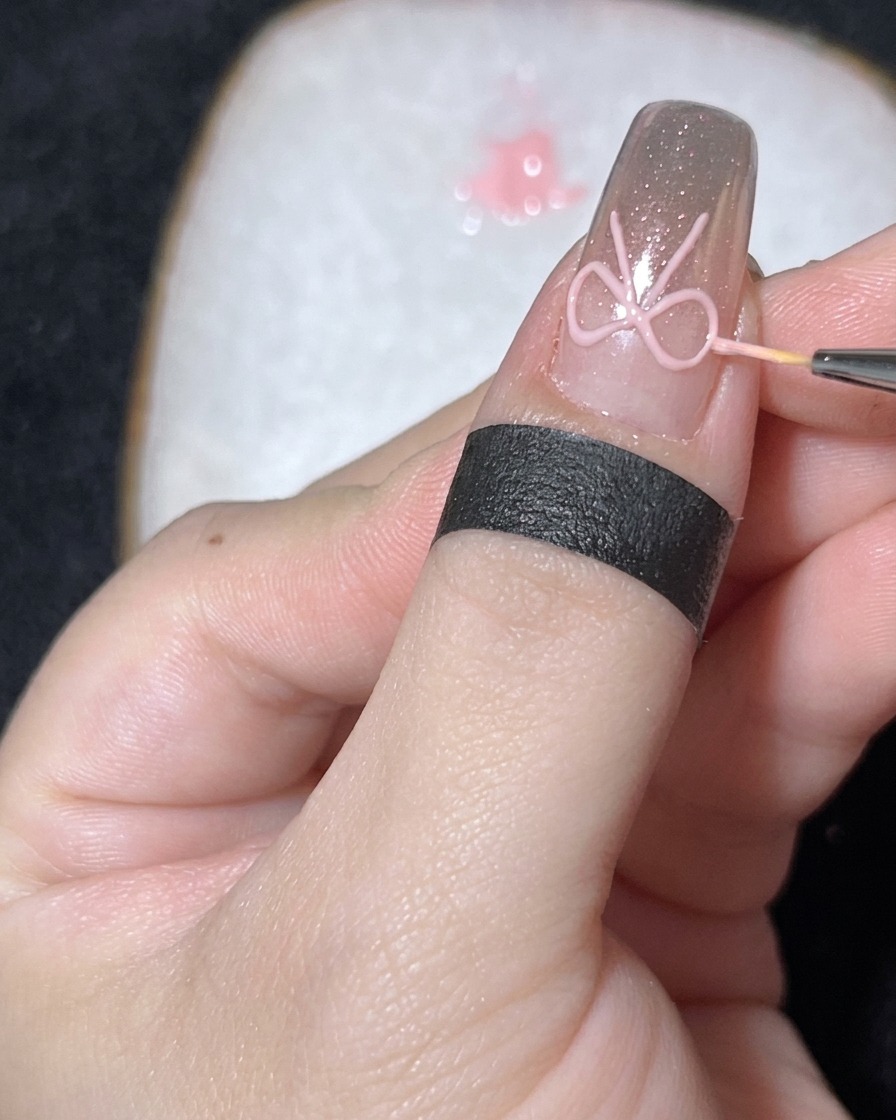 Primo piano di un pennello sottile che posiziona una piccola perla bianca al centro di un fiocco in gel 3D su ununghia cromata.