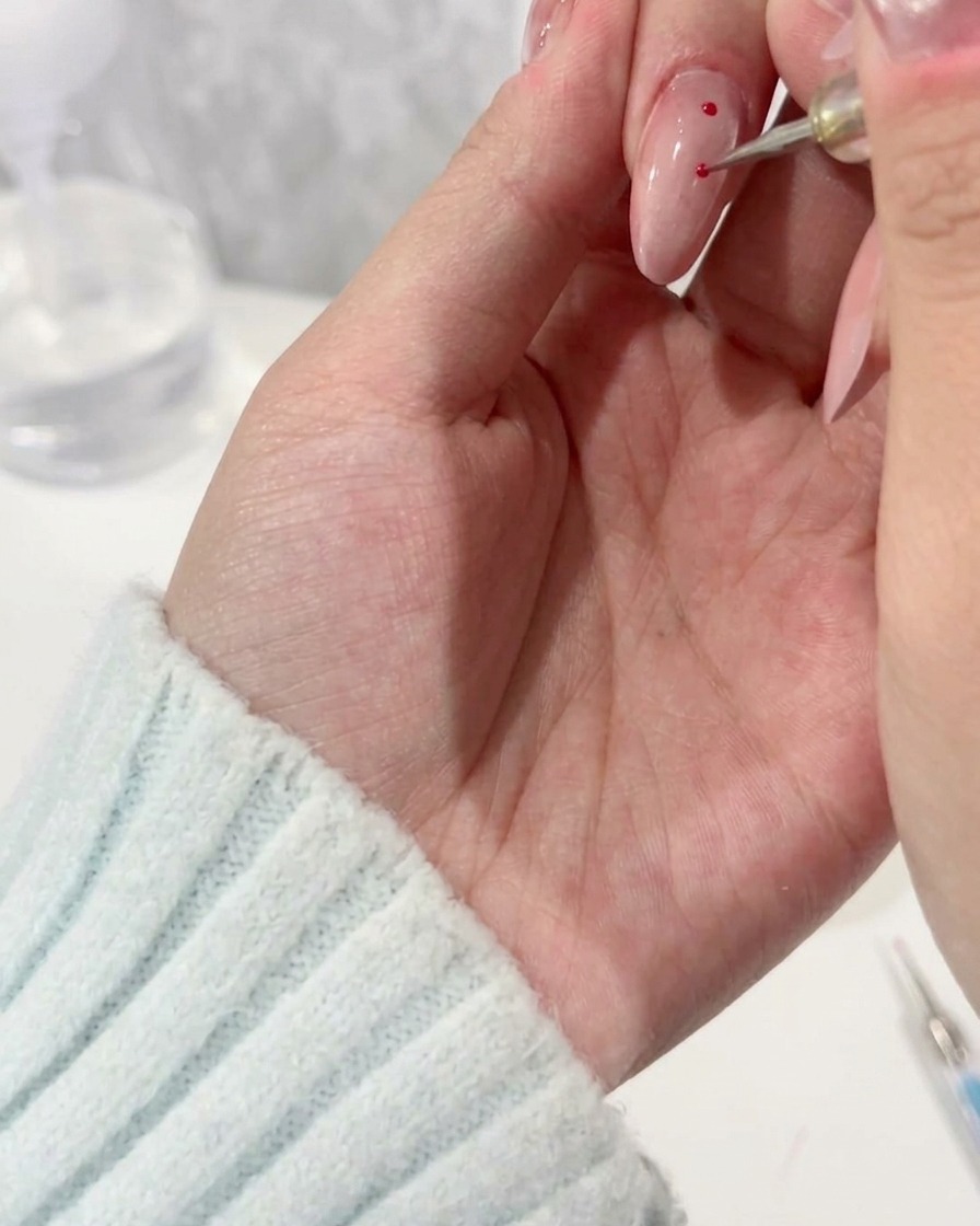 Un dotting tool applica precisi pois magenta su una base per unghie chiara.
