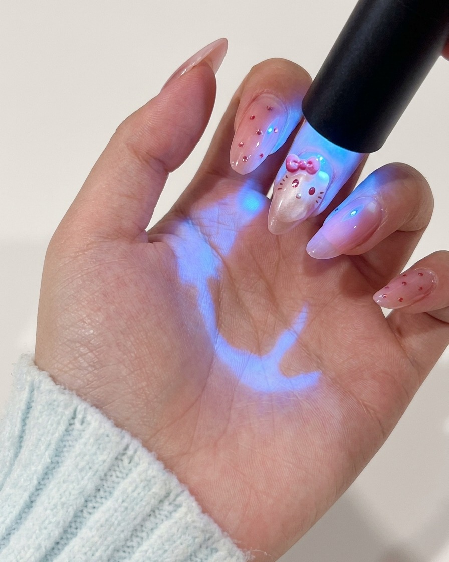 Una mano tiene una lampada UV sopra lunghia per polimerizzare il design dipinto del personaggio.