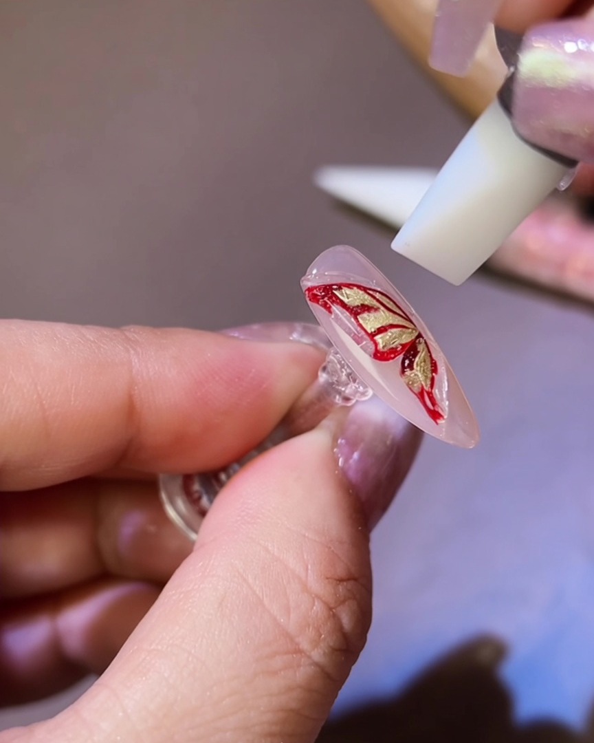 Uno strumento in silicone che modella il gel 3D nella silhouette di unala di farfalla sullunghia.
