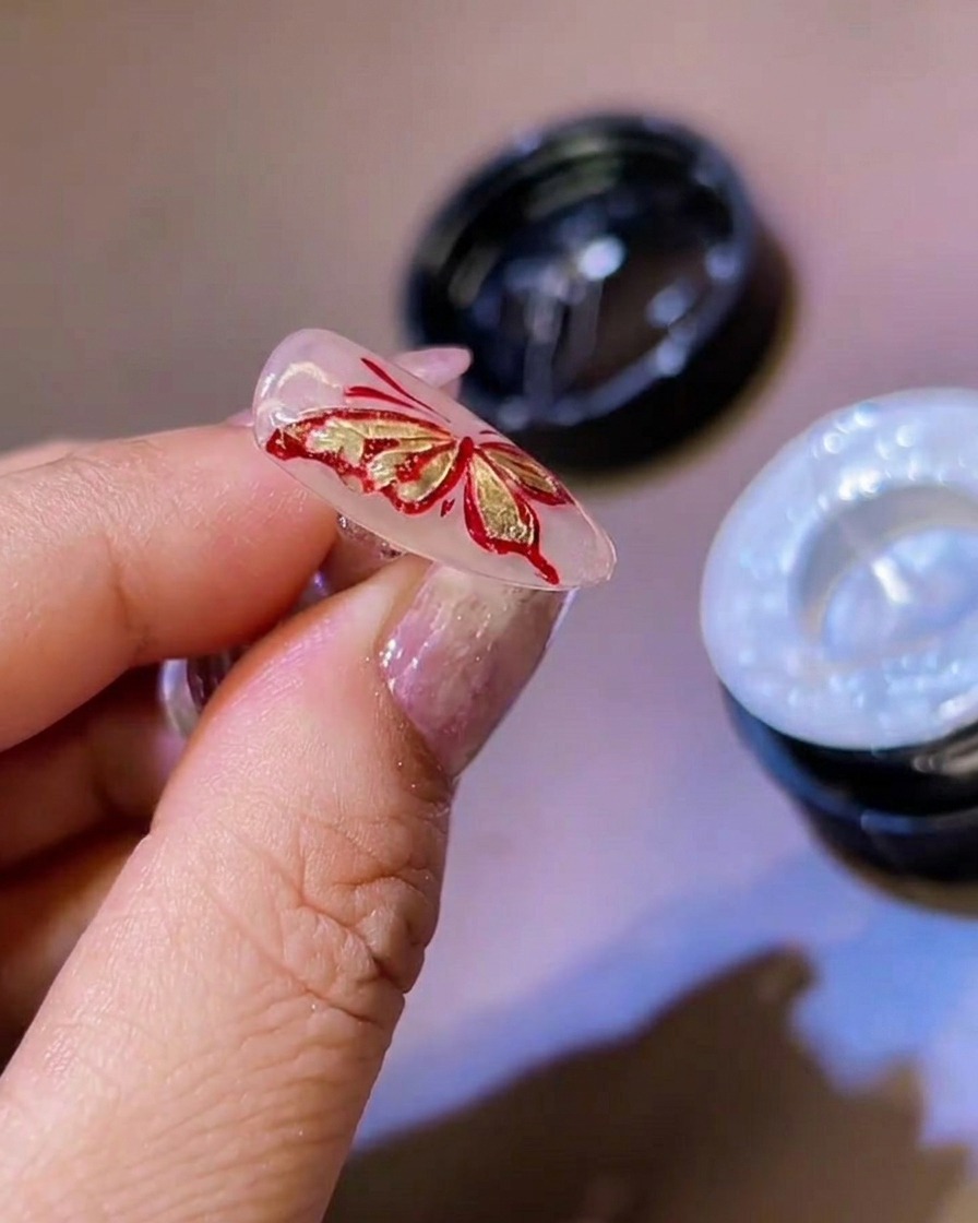 Un pennello a punta fine che aggiunge sottili dettagli in gel bianco ai bordi delle ali di farfalla 3D.