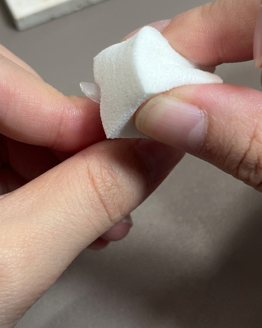 Primo piano di un pennello che applica uno smalto gel rosa traslucido su una punta di unghia.