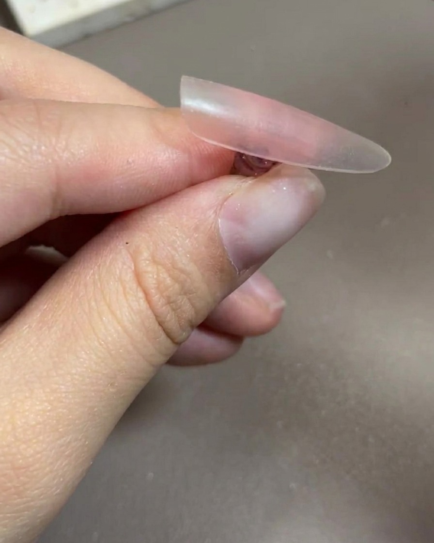 Una mano inserita in una lampada professionale per unghie UV/LED, con le unghie chiaramente visibili sotto la luce.