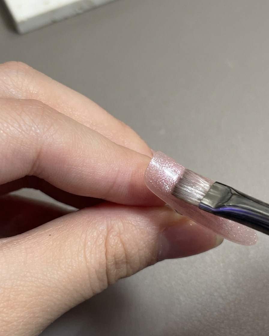 Un pennello piatto per gel che stende del gel magnetico cat-eye rosa scintillante sulla punta dellunghia.