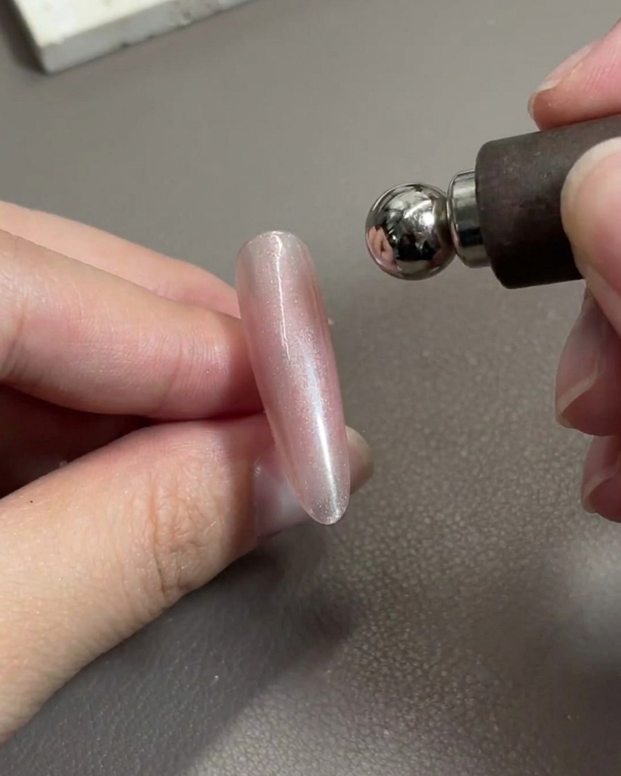Uno strumento magnetico per unghie posizionato sopra ununghia in gel rosa lucido, mentre sposta le particelle metalliche.