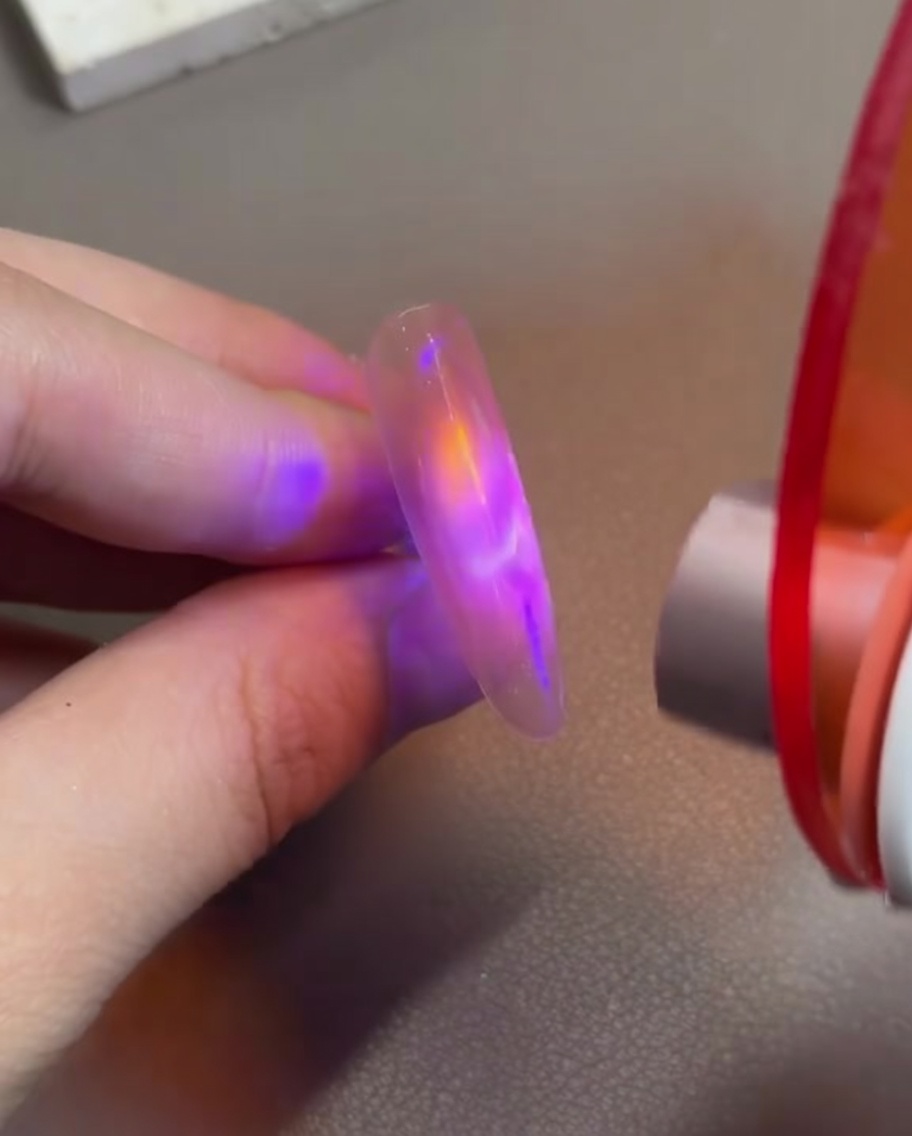 Un dito con gel cat-eye rosa che viene tenuto sotto una piccola lampada LED portatile per fissare il design magnetico.