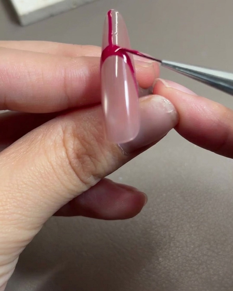 Un pennello per nail art che applica gel rosso rosa per riempire lo spazio allinterno del contorno della french.