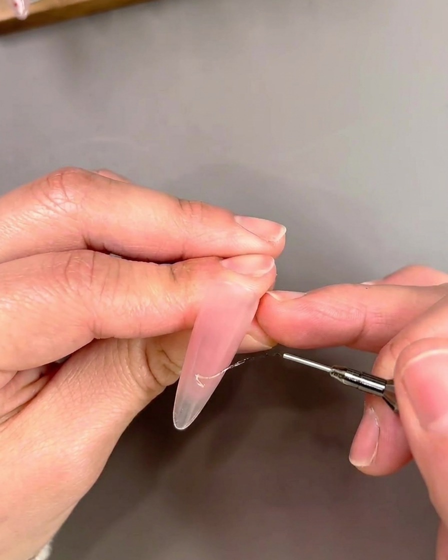 Un dettaglio di un pennello a punta sottile che applica gel cat-eye dorato in un design French tip.