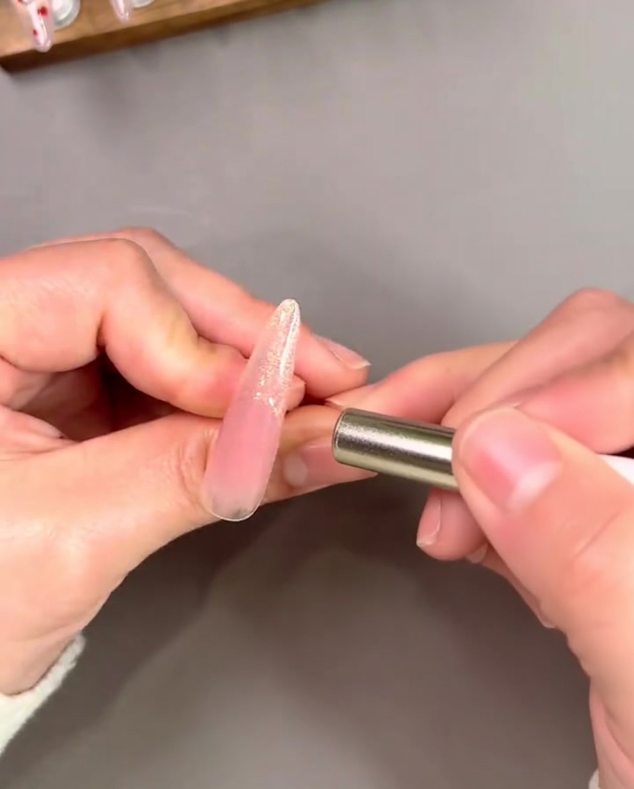 Un magnete tenuto vicino a una punta French dorata per creare un effetto cat-eye riflettente concentrato.