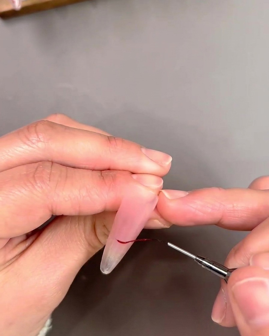 Un dettaglio di un pennello a punta sottile che contorna una punta French con una linea sottile di smalto gel rosso.