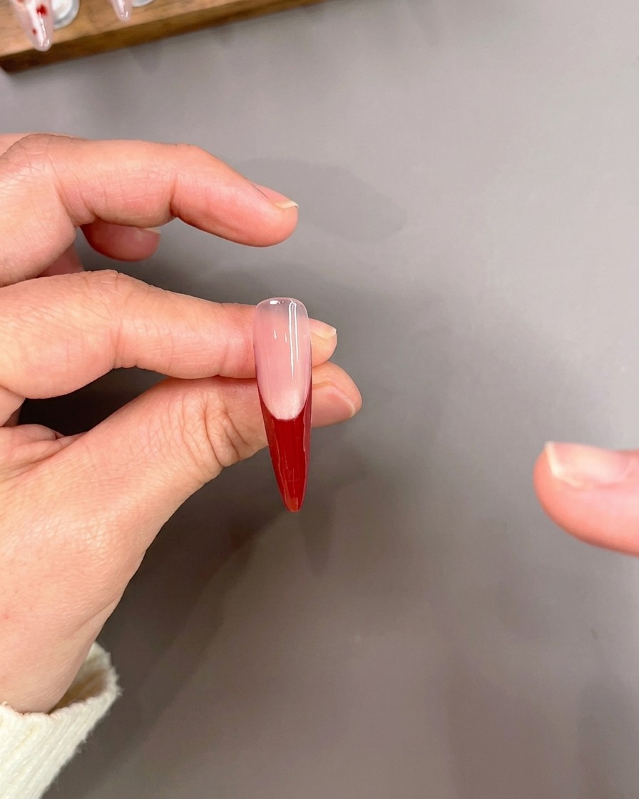 Un pennello a punta sottile che disegna con cura sottili linee rosse sulla punta di ununghia con base French manicure rossa.