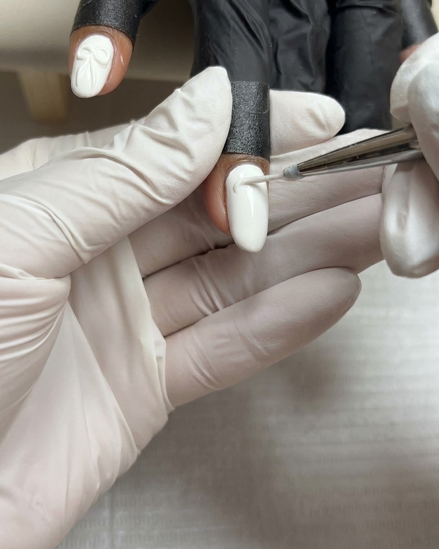 Una piccola e precisa goccia di denso gel scultoreo bianco posizionata al centro di ununghia dipinta di bianco.