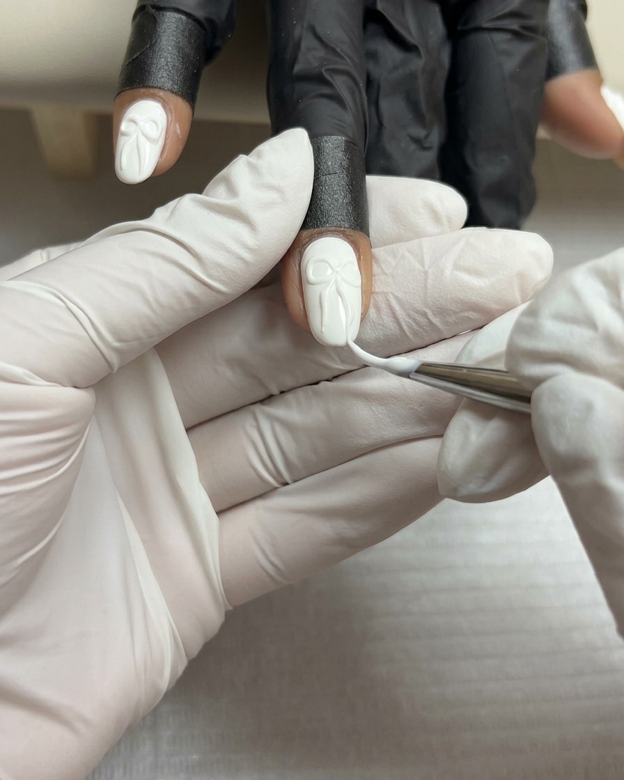 Primo piano di un pennello liner sottile che aggiunge linee bianche sottili sulla superficie di un fiocco in gel 3D su ununghia bianca.