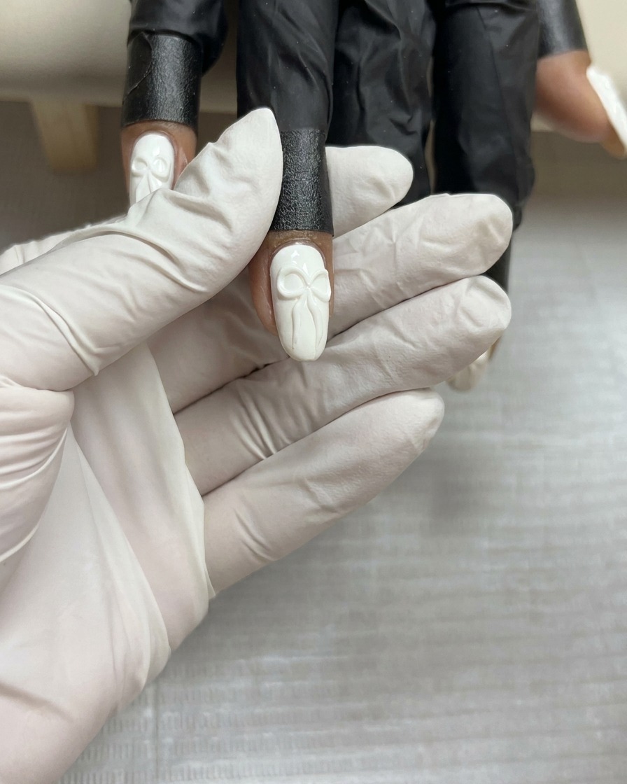 Vista dallalto di un design completato con fiocco in gel 3D su ununghia bianca, tenuta ferma prima della polimerizzazione finale.