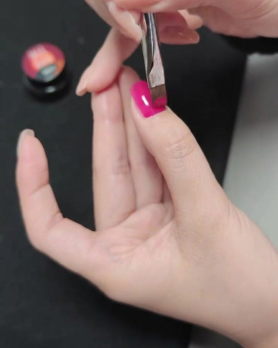 Un pennello stende una seconda passata di smalto gel magenta sullo strato precedentemente polimerizzato.