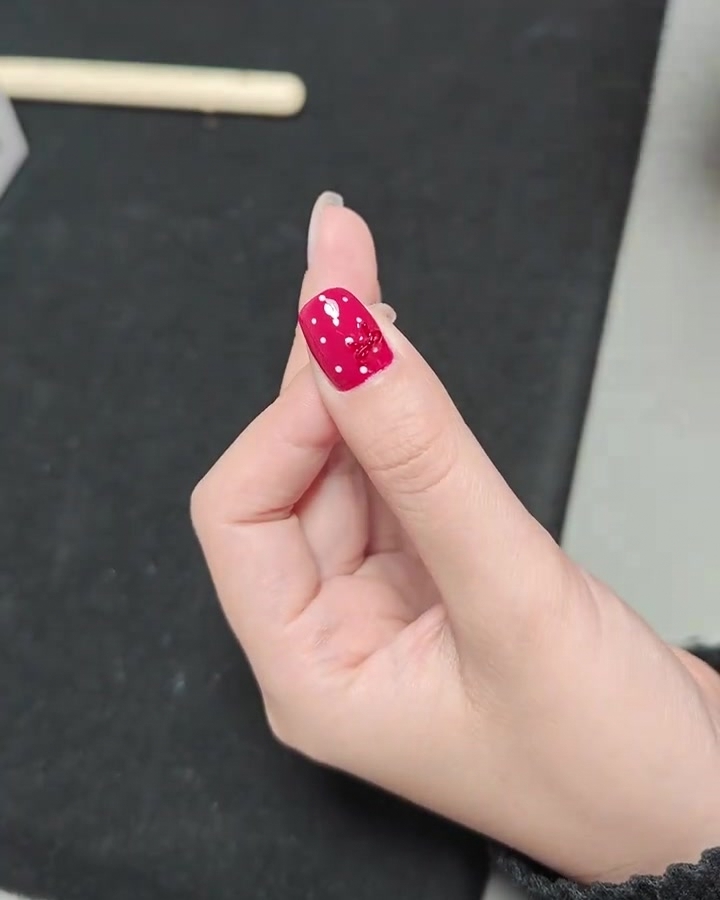Primo piano di una mano con la manicure a pois e fiocco rosso terminata, allinterno di una lampada UV professionale.